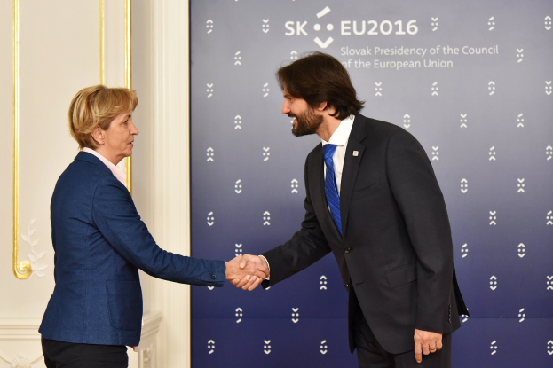 Bundeskanzlerin Angela Merkel und Bundeskanzler Joachim Gauck geben sich die Hand vor einer Wand mit einem "EU-Gipfel"-Schild und einer Tür im Hintergrund, beide lächeln.