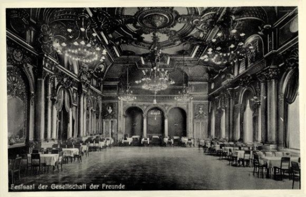 Schwarzes und weißes Foto eines großen Saals mit Tischen, Stühlen, Säulen, Bögen und Kronleuchtern; Text unten lautet "Festival der Gesellschaft der Freunde, Berlin".
