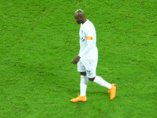 Ein Fußballspieler in einem weißen T-Shirt, weißen Shorts und orangefarbenen Schuhen läuft über ein saftig grünes Feld.