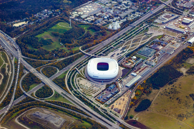 Luftaufnahme des Olympiagel"nde in M"unchen, Deutschland, umgeben von Geb"uden, B"umen, Stra"en, Fahrzeugen und Gras.