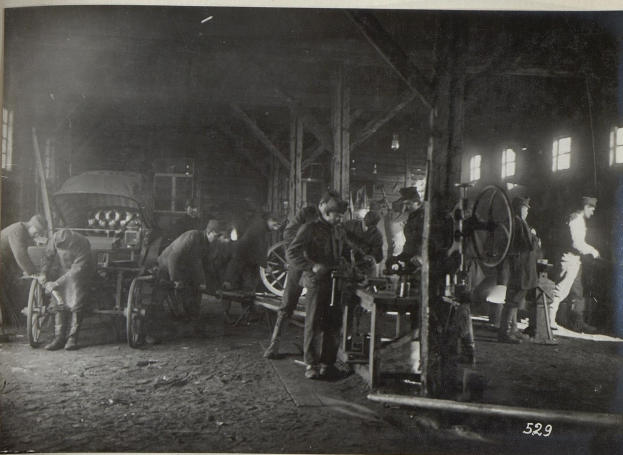 Schwarzes und weißes Foto von Männern, die in einer Fabrik arbeiten, mit einem Fahrzeug und Fenstern im Hintergrund.