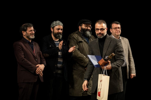 Eine Gruppe von Männern auf einer Bühne, einer hält eine Tüte und eine Trophäe, feiert die Eröffnungsnacht des Berliner Filmfestivals.
