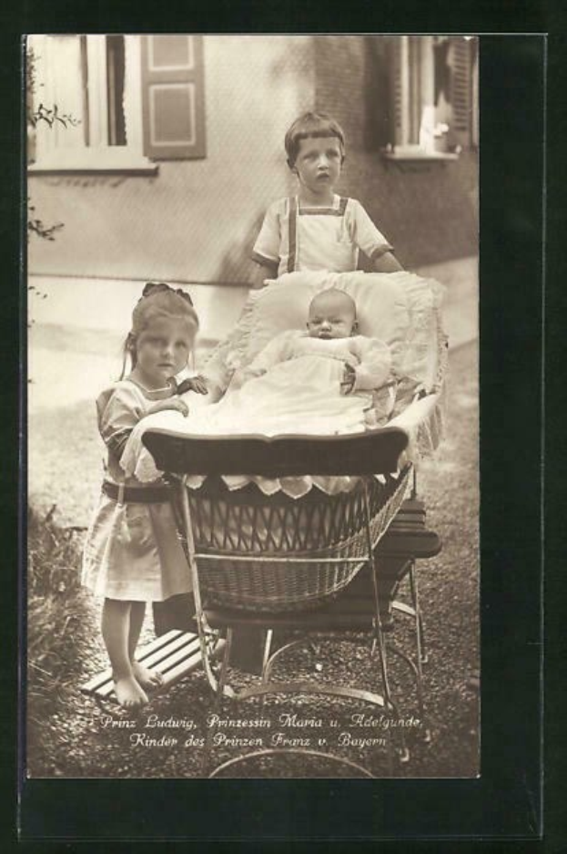 Schwarz-weiß-Foto von zwei Kindern, die neben einem Baby in einer Wiege stehen, mit einem Gebäude und einer Pflanze im Hintergrund und Text unten.