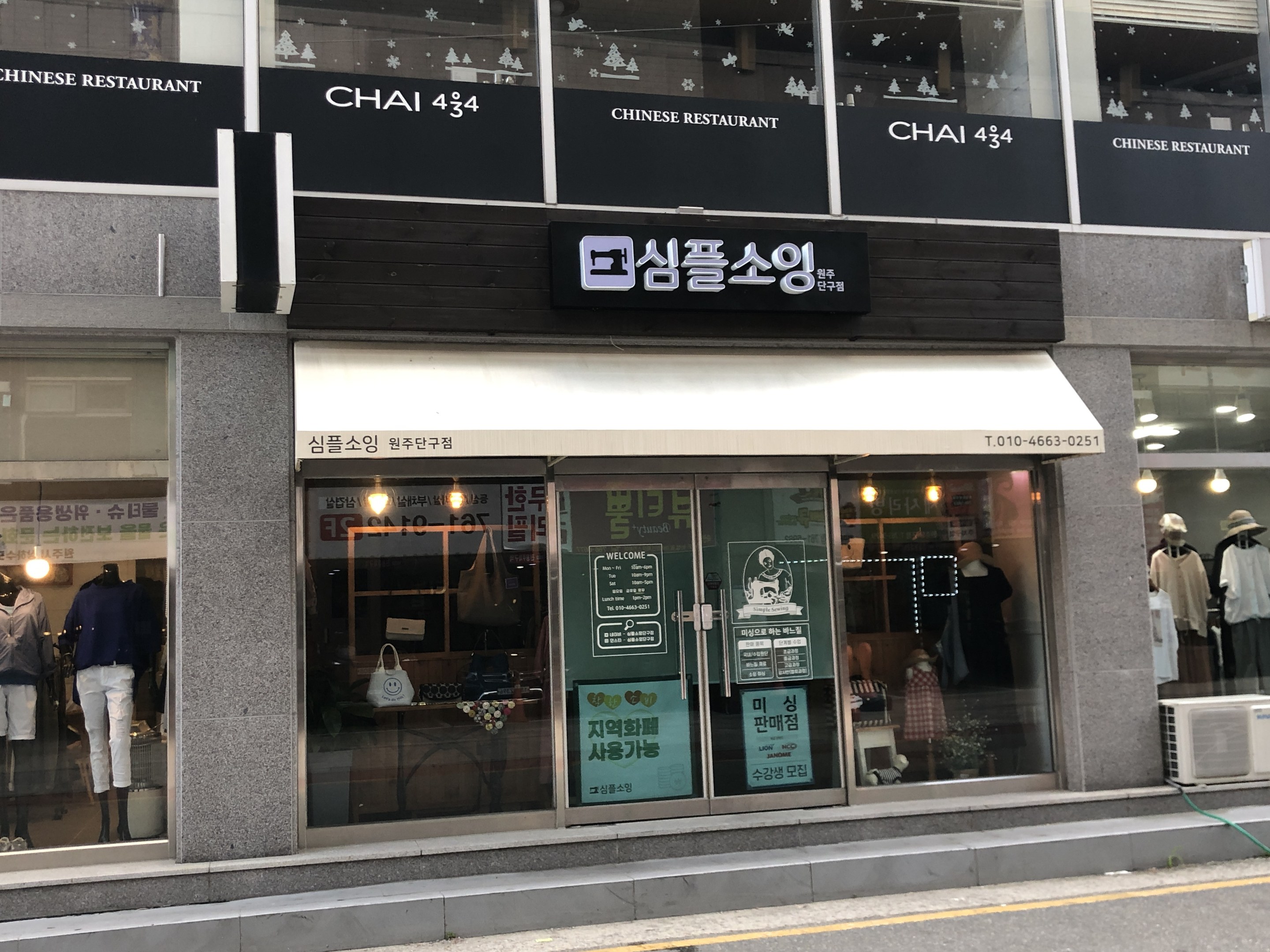 Außenansicht des Chai 434 Chinesischen Restaurants in Seoul, Südkorea, mit Glaswänden, Schaufensterpuppen in Kleidern, beleuchteten Schildern und einer Klimaanlage auf der rechten Seite, mit einer Straße unten.