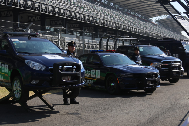 Polizeiautos vor einer Rennstrecke geparkt, uniformierte Personen und Stadion im Hintergrund