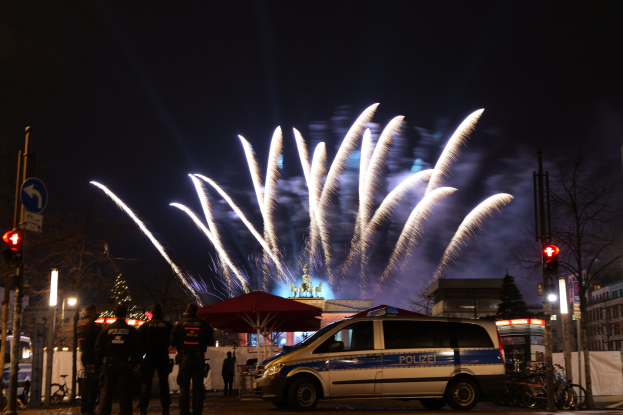 Polizeifahrzeug vor Menschenmenge mit farbigen Feuerwerken am nächtlichen Himmel.