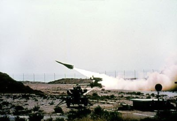 Eine Rakete, die von einem Militärfahrzeug in einer Wüstenlandschaft mit Vegetation, einem Zaun und einem Himmel im Hintergrund gestartet wird.