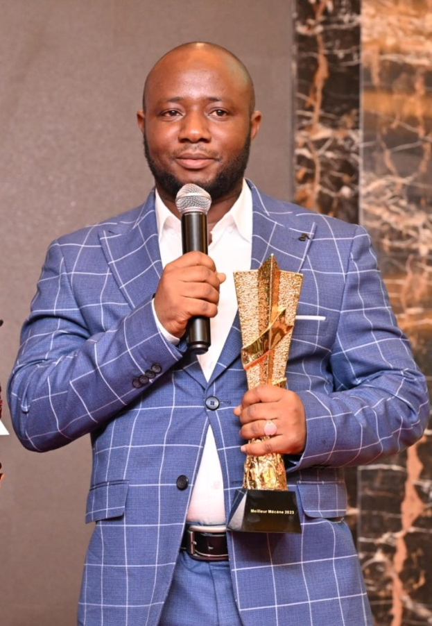 Ein Mann in einem blauen Anzug mit Mikrofon und Trophäe, der fröhlich und selbstbewusst feiert.