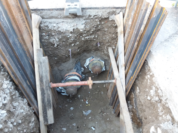 Großes Loch auf einer Baustelle umgeben von Metallstangen und Steinen, mit einem Fahrzeug oben.