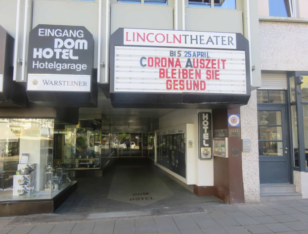 Außenansicht des Lincoln Theaters in Berlin, Deutschland, mit Glasfenstern und -türen sowie einer Schautafel und einem Blick ins Innere, der eine belebte städtische Umgebung vermuten lässt.