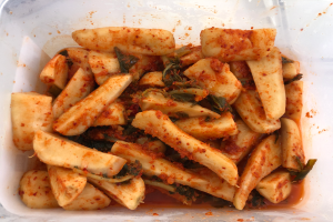 Ein Plastikbehälter voller goldbraun gebratener Tofu und farbenfroher Gemüse, darunter grün, gelb und rot, auf einem Tisch.