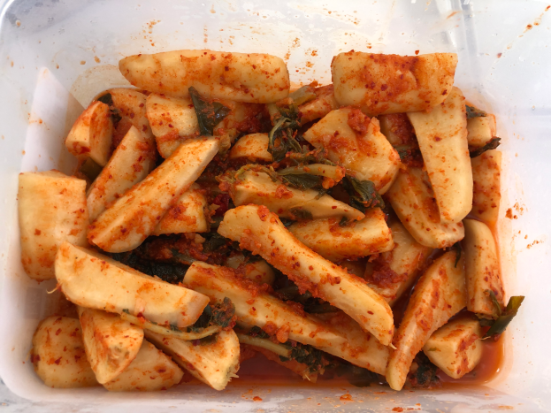 Ein Plastikbehälter voller goldbraun gebratener Tofu und farbenfroher Gemüse, darunter grün, gelb und rot, auf einem Tisch.