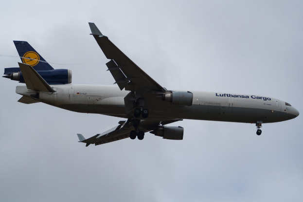 Ein Lufthansa Cargo Boeing 777-300ER im Flug, mit ausgefahrenen Flügeln und aktivierten Triebwerken, mit sichtbarem Text auf seinem Rumpf gegen einen bewölkten Himmel.