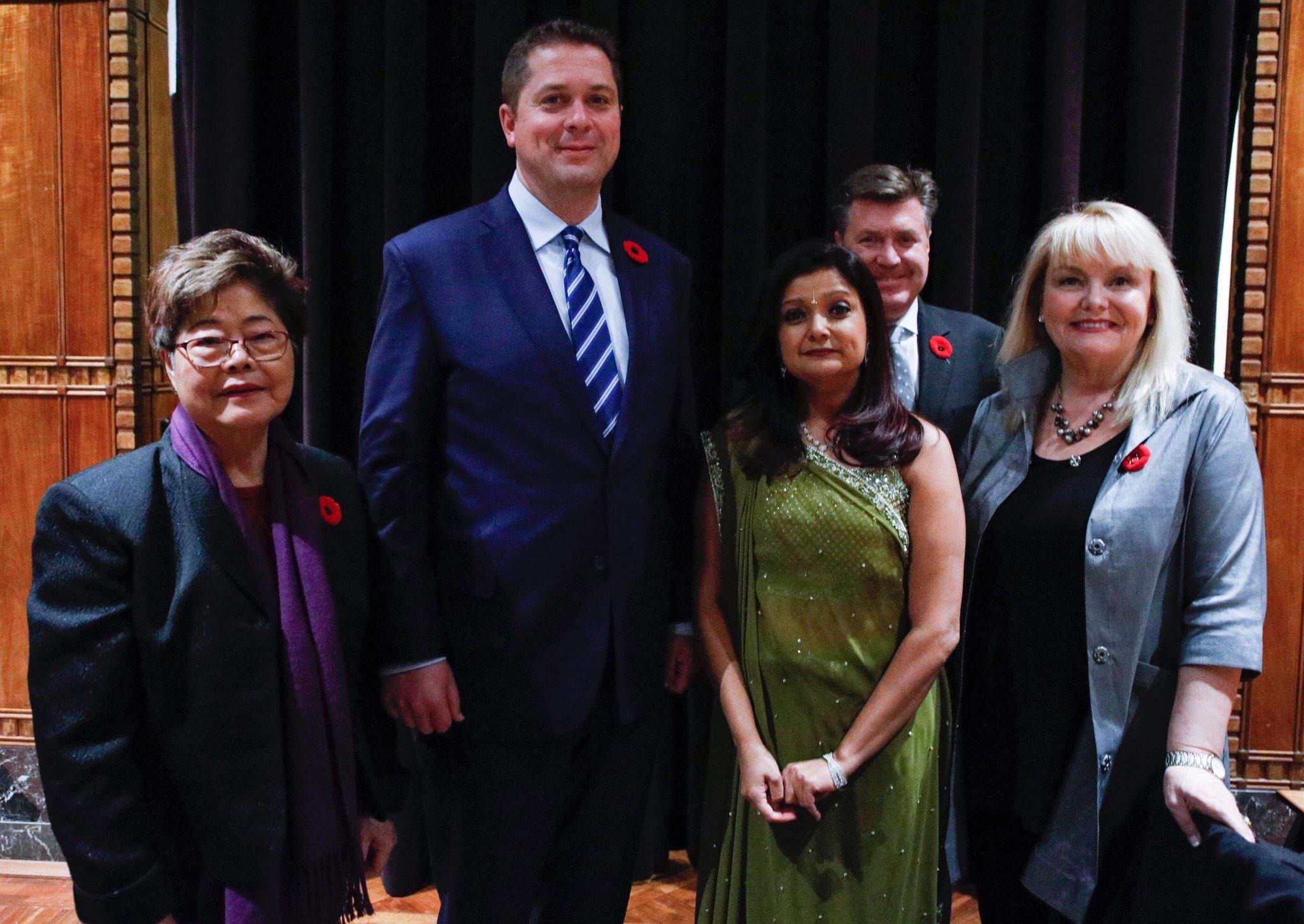 Eine Gruppe von Liberalen, die vor einem schwarzen Vorhang mit einer hölzernen Wand im Hintergrund zusammenstehen.