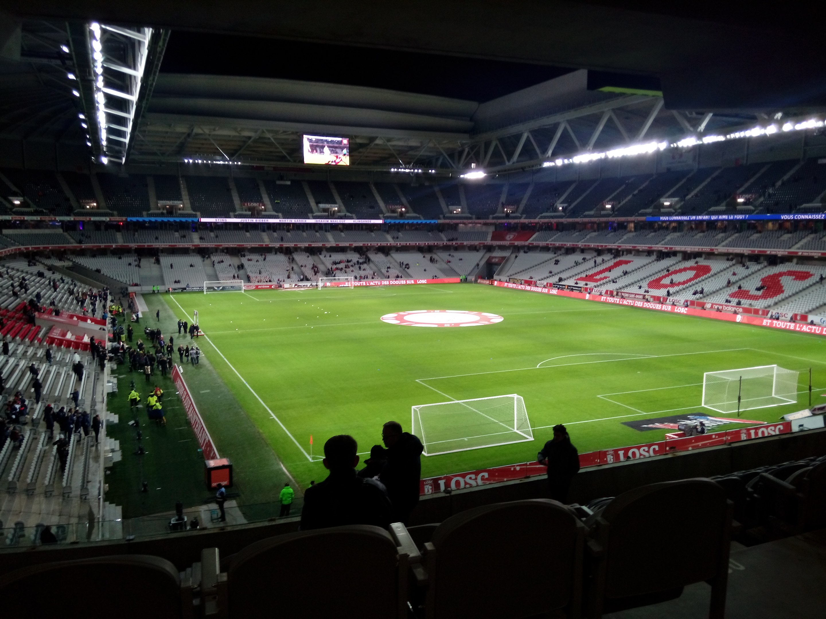 Ein großes beleuchtetes Stadion, Estadio Santiago Bernabéu, voller Zuschauer bei einem Fußballspiel, einige sitzen und andere stehen, mit einem großen Bildschirm oben.