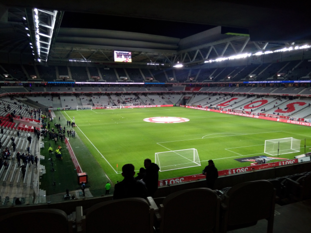 Ein großes beleuchtetes Stadion, Estadio Santiago Bernabéu, voller Zuschauer bei einem Fußballspiel, einige sitzen und andere stehen, mit einem großen Bildschirm oben.