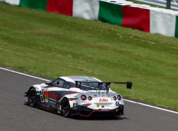 Ein Nissan GT-R Nismo GT3 Rennauto auf der Nürburgring 24 Stunden Strecke, mit grünem Gras und einem Zaun im Hintergrund.