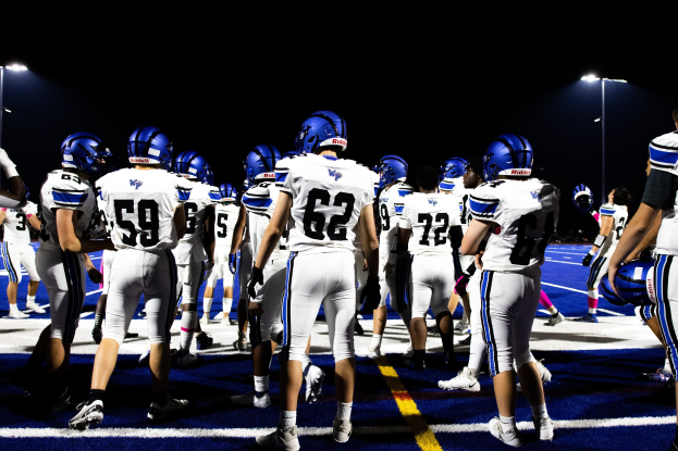 Eine Gruppe von Fußballspielern in Helmen und Stollenschuhen auf einem Feld unter Flutlicht, bereit für ein Spiel.