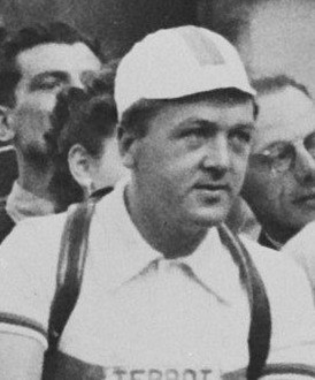 Schwarzes und weißes Foto eines Mannes in einer Mütze und Hosenträgern, der vor einer Menge steht, wahrscheinlich als Darstellung der legendären Karriere eines Fußballspieler.