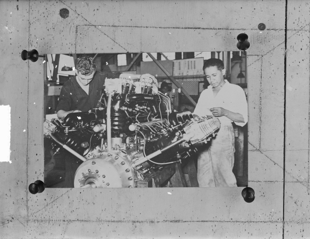 Zwei Männer in einer Fabrik untersuchen ein Flugzeugtriebwerk auf einem Schwarz-Weiß-Foto.