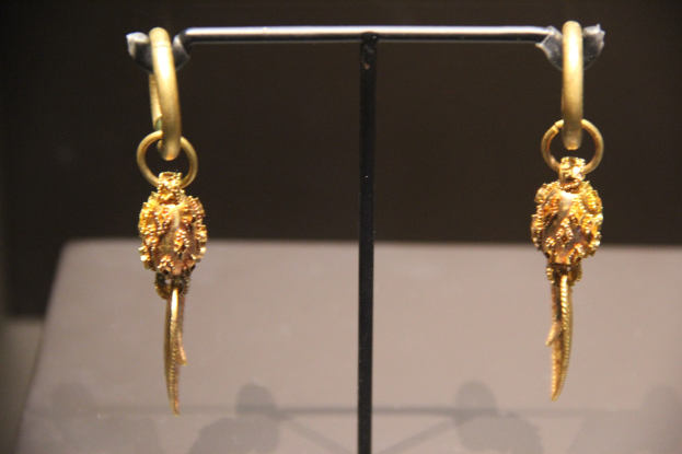 Goldene Ohrringe auf einem St├Ąnderchen in einer Glasvitrine mit unscharfem Hintergrund.