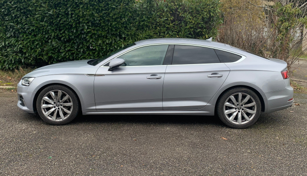 Grauer Audi A5 Sportback 2.0 TDI Quattro Tiptronic S Tronic S Line 5dr Diesel Estate auf einer Straße mit Bäumen und einem Gebäude im Hintergrund.