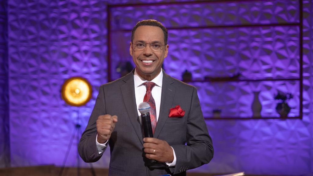 Stephen Colbert, Moderator von 'The Daily Show with Trevor Noah', steht auf einer Bühne und hält ein Mikrofon in der Hand, trägt einen Anzug, Krawatte und Brille, mit einem Scheinwerfer und Ständer im Hintergrund.