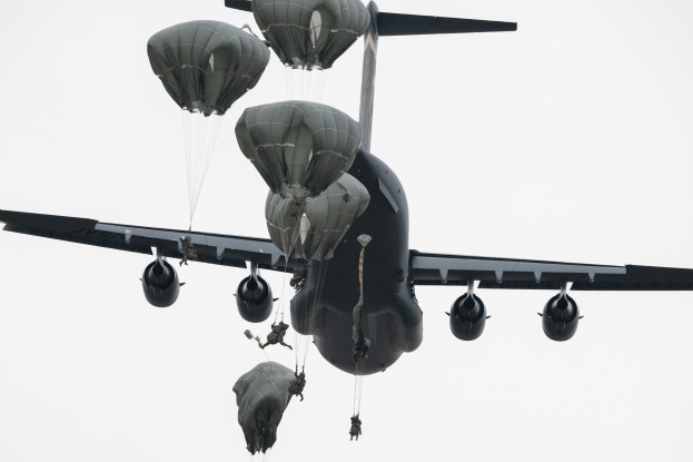 Ein großes Militärflugzeug mit mehreren Fallschirmen, das gegen einen klaren blauen Himmel fliegt.