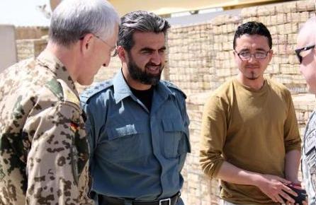 Eine Gruppe von Männern steht vor einer Backsteinwand, einer hält ein Objekt, während der Mann in der Mitte von der irakischen Armee interviewt wird, was darauf hindeutet, dass er der US-Verteidigungsminister ist.