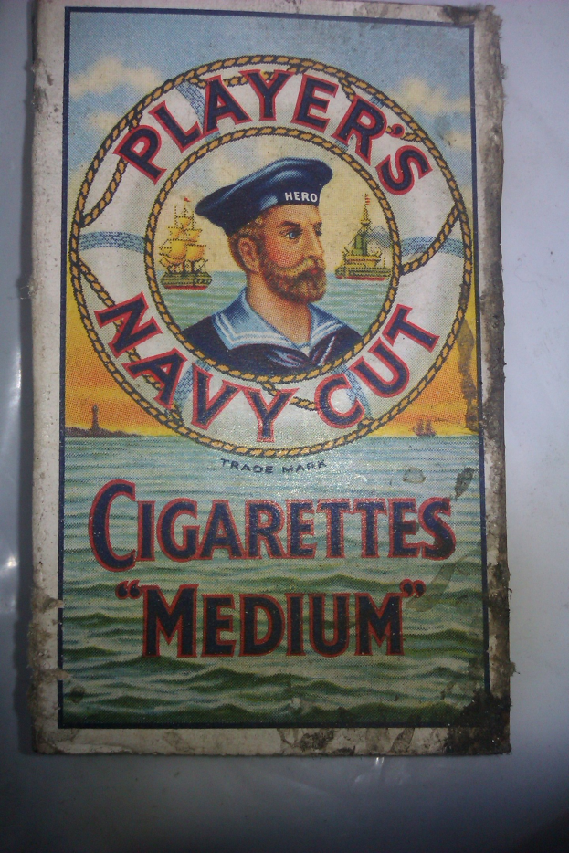 Plakat mit einer Person in einer marineblauen Uniform mit weißem Hemd und roter Krawatte, die Arme verschränkt und einen strengen Gesichtsausdruck hat, wirbt für "Player's Navy Cut Cigarettes Medium" in fetter schwarzer Schrift innerhalb eines weißen Randes.