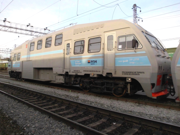 Eine diesel-elektrische Lokomotive fährt neben einem anderen Zug auf parallelen Gleisen, mit elektrischen Masten und Oberleitungen im Hintergrund unter einem klaren blauen Himmel.