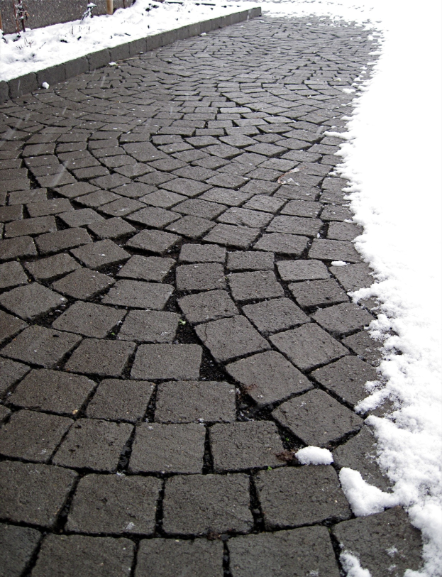 Eine Kopfsteinpflasterstraße mit leichtem Schnee und einem Hintergrundzaun.