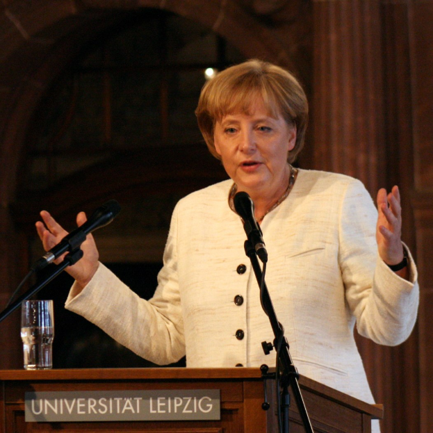 Bundeskanzlerin Angela Merkel hält eine Rede an der Universität Leipzig, stehend hinter einem Rednerpult mit einem Mikrofon und einem Glas Wasser.