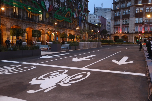 Stadtstraße mit einem ausgewiesenen Radweg, umgeben von Gebäuden, Straßenmöblierung, Fußgängern auf dem Gehweg und einem klaren blauen Himmel.