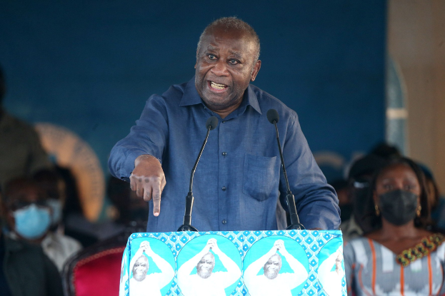 Ein Mann in einem blauen Hemd spricht in zwei Mikrofone an einem Rednerpult, während ein sitzendes Publikum hinter ihm zuhört.