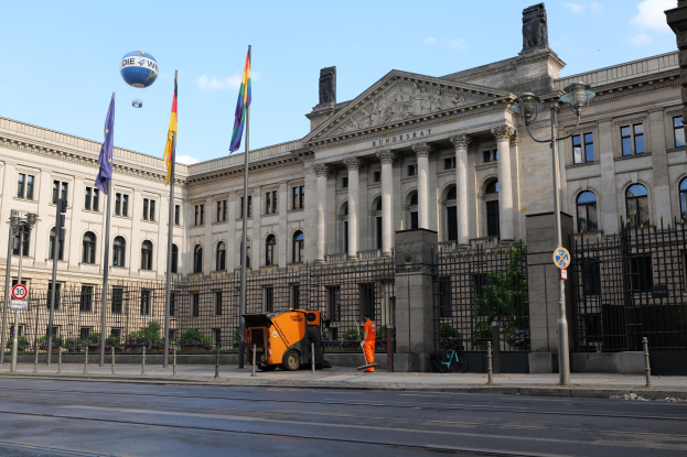 Großer moderner Bau mit vielen Fenstern, als Bundestag in Berlin, Deutschland identifiziert, umgeben von Straßeninfrastruktur, Fahrzeugen, Passanten und Bäumen unter einem bewölktem Himmel.