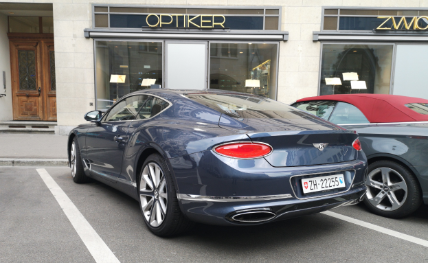 Ein schwarzer Bentley Continental GT V8 S, der auf einer Straße vor einem modernen Gebäude mit Glaswänden und -türen geparkt ist, mit Text und Papieren auf dem Glas.