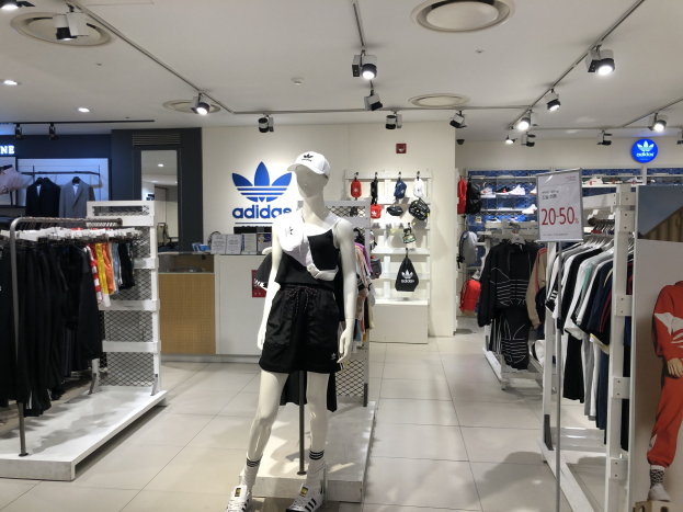 Innenraum eines adidas-Ladens in Singapur mit Schaufensterpuppen, Kleiderständern, einer Texttafel auf der rechten Seite und Deckenbeleuchtung.