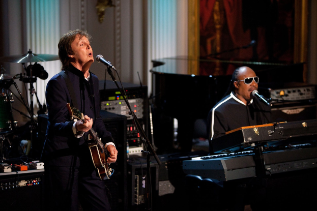Paul McCartney und Stevie Wonder performen gemeinsam auf der Bühne bei den Grammys, wobei McCartney Gitarre spielt und singt und Wonder eine Brille trägt, während er am Piano spielt.