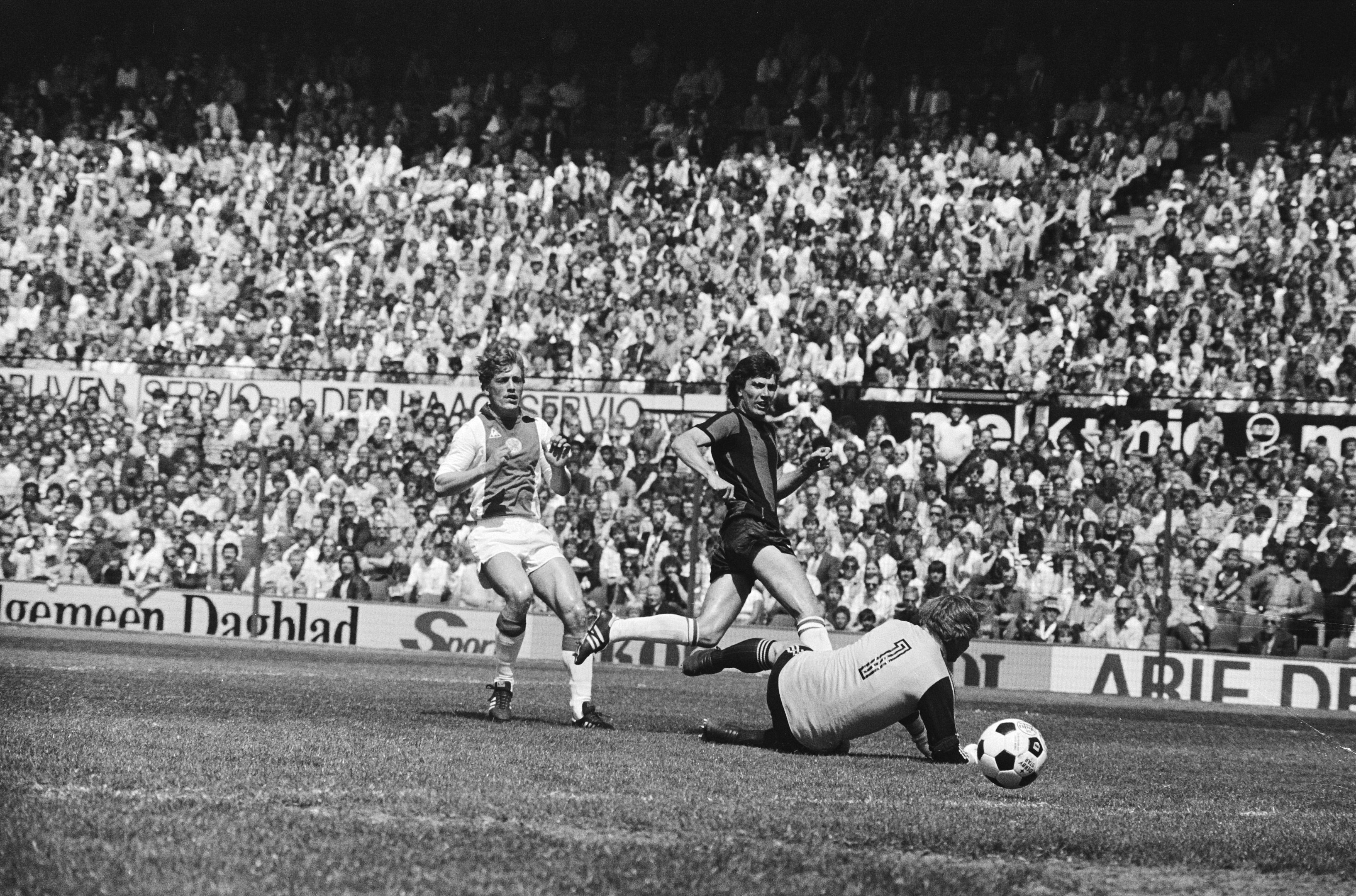Schwarzes und weißes Foto von Fußballspielern im Einsatz auf einem Feld mit Zuschauern im Hintergrund und einer Bundesliga 1978-79-Match-Banner.
