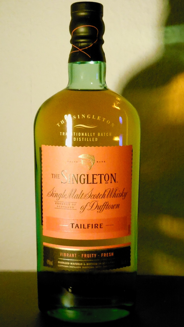 Eine tiefe bernsteinfarbene Flasche Singleton of Dufftown Tailfire Single Malt Scotch Whisky mit einem schwarzen Etikett, das eine Schrift in fetter schwarzer Schrift und ein Wappen mit einem Löwen und einem Schloss zeigt.