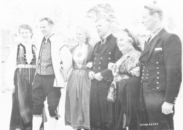 Schwarzes und weißes Foto einer lachenden Gruppe von Menschen, die draußen neben Bäumen stehen, mit der Beschriftung "Bayerische Familie in den 1930er Jahren" unten.