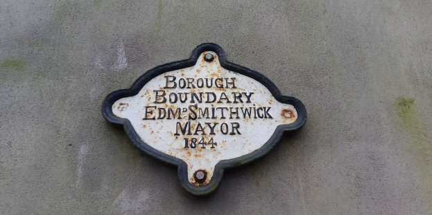 Schwarze Metalltafel an einem Gebäude mit weißer "Borough Boundary Edm Smithwick Mayor"-Aufschrift in fetter Schrift.