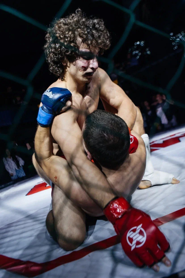 Zwei Männer in einem MMA-Ring im Kampf, wobei einer einen mächtigen Tritt gegen den anderen landet.