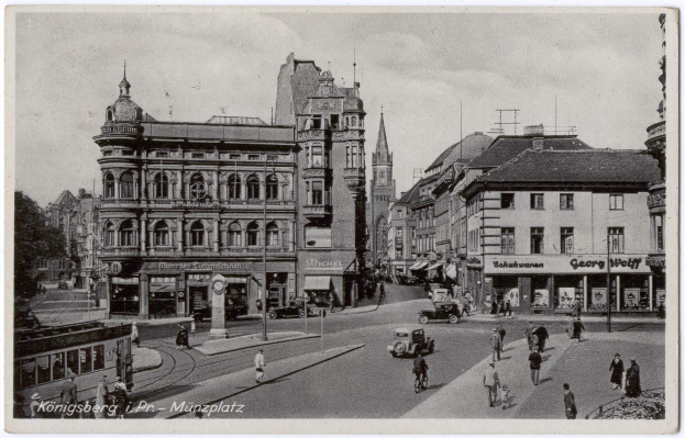 Schwarz-weißes Foto einer belebten Münchner Stadtstraße mit Fußgängern, Fahrzeugen und Fenstern gesäumten Gebäuden, Bäumen im Hintergrund und Text am unteren Rand.