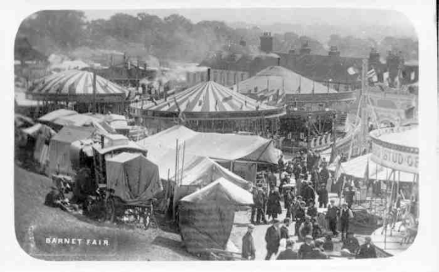 Schwarz-weiß-Foto von Barnet Fair in London, England, mit Zelten, Menschen, Karren, Pfählen, Bäumen und Gebäuden im Hintergrund.
