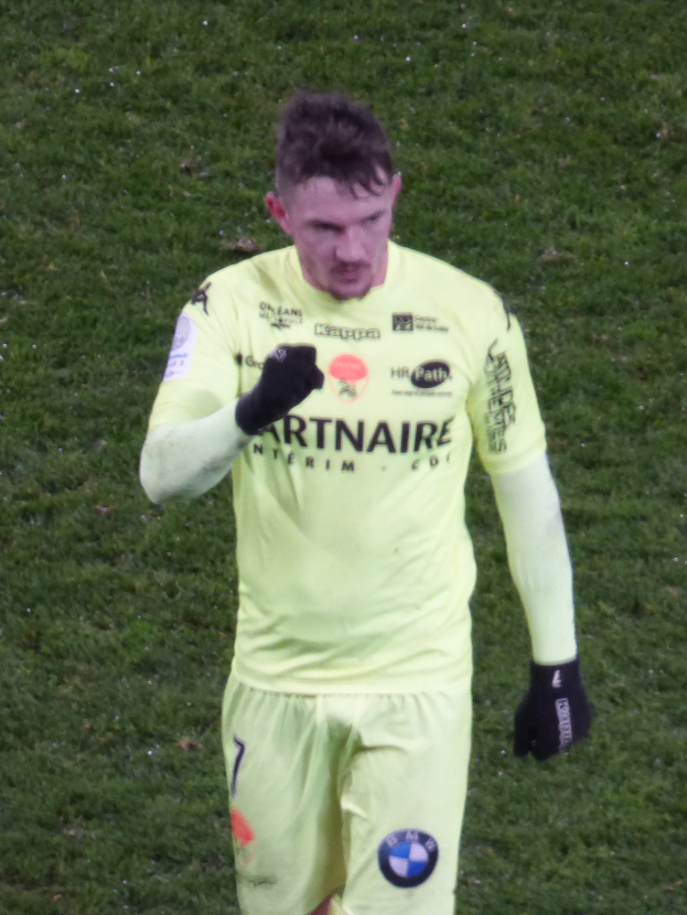 Ein Torwart in einem gelben Trikot steht auf einem Fußballfeld und trägt eine gelbe T-Shirt, Shorts und schwarze Handschuhe.