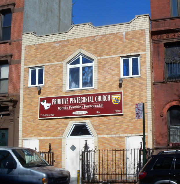Außenansicht eines Gebäudes mit einer Tafel, die 'Primitive Pentecostal Church in Philadelphia, Pennsylvania' lautet, einem Metallzaun, Fahrzeugen auf der Straße und einem bewölkten Himmel.