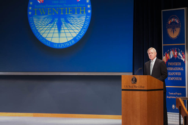 US-Außenminister Mike Pompeo trägt einen schwarzen Blazer, ein weißes Hemd und eine schwarze Krawatte und steht an einem Podium mit zwei Mikrofonen, während er auf der 20. Internationalen Seapower Symposium vor einem blauen Hintergrund und einem Geländer zur Rechten spricht.