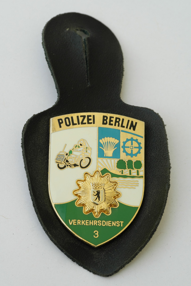 Polizei Berlin Abzeichen mit einem blauen Schild, weißer Stern und schwarzer Schrift auf einem weißen Rand, auf einer Oberfläche platziert.